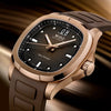 A close-up of the Mido Watches Multifort TV Big Date M0495263304100, showcasing a rose gold case, brown textured dial with bold hour markers, date display, and a brown rubber strap against a blurred golden background.