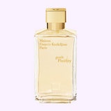 A Maison Francis Kurkdjian Gentle Fluidity Gold 6.8 EDP Sp Unisex perfume bottle with a gold cap and lettering sits against a light pink background, showcasing the luxury of Maison Francis Kurkdjian Paris Perfumes.