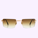 Maybach Optical THE WOLF I MG-AB-M09: Rectangular, rimless sunglasses with a gold nose bridge and temples, featuring brown gradient tinted lenses set against a solid light purple background.