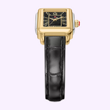 The Michele Watches Deco Madison Mini MWW06D000179, a gold and silver rectangular wristwatch featuring a black dial with Roman numerals and a black leather strap from the elegant Michele Watches collection, is displayed vertically on a light background.