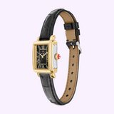 Showcasing timeless elegance, the Michele Watches Deco Madison Mini MWW06D000179 features a rectangular gold and silver case with a striking black dial, Roman numerals, and Michele’s distinctive red winding crown. This sophisticated black leather watch by Michele Watches is beautifully displayed against a light purple background.