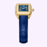 The Michele Watches Deco Madison Mini MWW06D000180 features a gold square case, a blue dial with Roman numerals, and a navy leather strap, elegantly photographed on a light background.