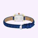 A blue leather Michele Watches Deco Madison Mini MWW06D000180 is shown from the back, highlighting its gold and silver case with Michele Watches branding and details, set against a light purple background. This elegant timepiece features a classic navy leather strap for timeless appeal.