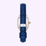 Certainly! Here’s the sentence rewritten using the given product data: A blue leather watch strap reminiscent of the Michele Watches Deco Madison Mini MWW06D000180, featuring a silver clasp and gold watch casing, is viewed from the back against a light purple background.