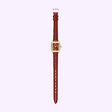 The Michele Watches Deco Madison Mini MWW06D000181 features a gold case with a square red face and a matching textured ruby red leather strap. Displayed vertically against a pale lavender background, this timepiece by Michele Watches radiates modern elegance.