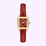 A Michele Watches Deco Madison Mini MWW06D000181 rectangular wristwatch by Michele Watches, featuring a gold and silver case, a ruby red leather strap, and a red face with Roman numerals, displayed on a light purple background.