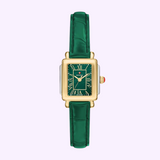 The Michele Watches Deco Madison Mini MWW06D000182 is a stunning rectangular gold watch with a green dial, Roman numerals, and an elegant green leather strap. Shown against a light purple background, this sophisticated timepiece also features a crown accented with bold red.