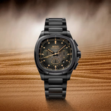 The Mido Watches Multifort TV Chronograph (M0495273308100) features a dark dial with gold accents and 60-hour power reserve, showcased upright on desert sand against a hazy sky—demonstrating Swiss engineering elegance.
