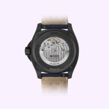 The Mido Watches Multifort TV Big Date M0495263704100 features a transparent caseback revealing its automatic movement, a black case, and a beige leather strap with visible stitching and inscribed model details.