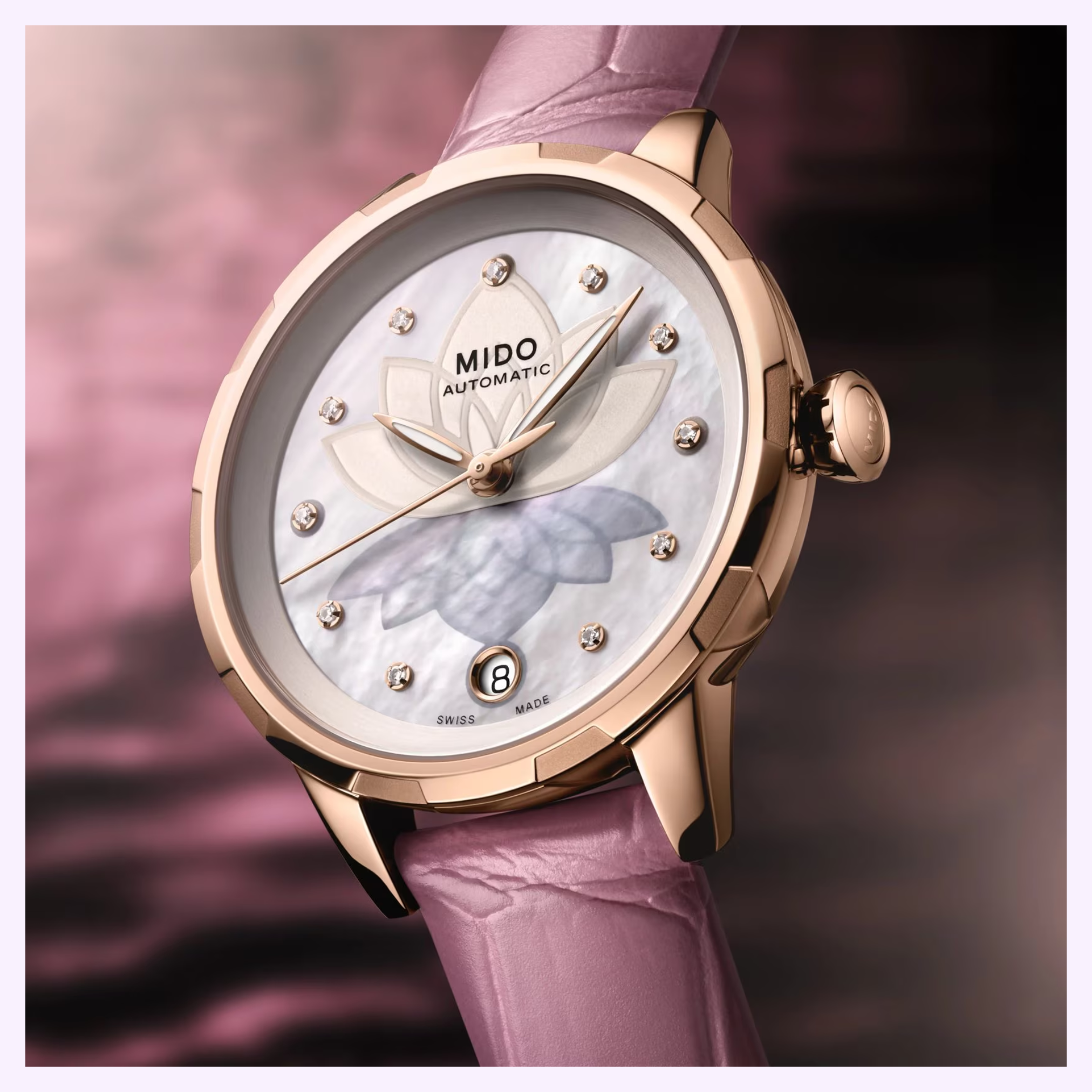 The Mido Watches Rainflower Night M0432073610600, featuring automatic movement, a pink leather strap, mother-of-pearl dial with diamond markers, floral motif, and date at 6 o'clock, is displayed against a blurred pink background.