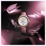 The Mido Watches Rainflower Night M0432073610600, featuring a pink mother-of-pearl dial and diamond markers, is showcased against a dreamy pink backdrop with lotus motifs and reflective water, highlighting this elegant Swiss women’s timepiece.