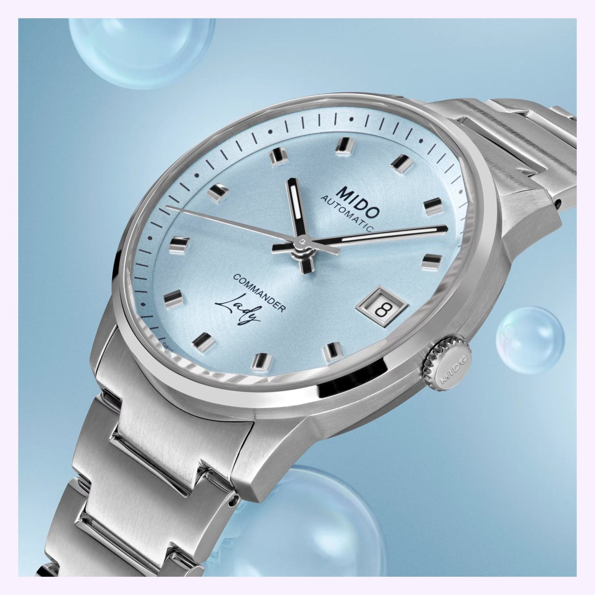 A close-up of the Mido Watches Commander Lady M0212071104100, a Swiss automatic watch with a light blue dial, date display, and silver markers by Mido Watches, set against a blue background with bubbles.