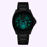 The Mido Watches Multifort TV Big Date Alebrijes M0495261108102 features a glowing turquoise skull on a black face, metal link band, luminous accents, and Caliber 80 automatic movement, set against a light purple background.