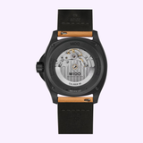A close-up of the Mido Watches Multifort TV Big Date M0495263608100 showcases its transparent case back, revealing the inner mechanical movement labeled Caliber 80. This timepiece by Mido Watches features a black case and a leather strap.