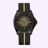 A Mido Watches Multifort TV Big Date M0495263608100 automatic wristwatch from Mido Watches, featuring a round face with gold hands and indices. The black fabric strap showcases a single gold stripe down the center, and the watch is displayed against a light purple background.