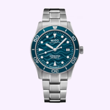 The Mido Watches Ocean Star 39 M0269071104101 features a teal blue dial, luminous markers, date at 3 o’clock, and a stainless steel bracelet, shown against a light purple background.