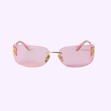 The Miu Miu Sunglasses 0MU A51S 5AK90Y75 from Miu Miu Sunglasses feature a pink rimless design with gold detailing, pink arms, and a gold bridge, showcased against a light purple background—an ideal choice for those looking for chic designer women’s eyewear.