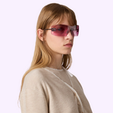 A person wears Miu Miu Sunglasses 0MU B53S 1BC70Y44, which are authentic, rimless shield-style sunglasses with pink tinted lenses and silver metallic details on the temples.