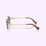 Miu Miu sunglasses 0MU 52YS ZVN80Q54 by Miu Miu Sunglasses, featuring gold frames and brown, curved temple tips, are displayed from the side against a light background. The authentic design is distinguished by unique decorative accents near the hinges.
