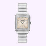 The Movado Watches 3650251 Heritage 1917 features a square face, silver metal band, light pink dial, silver markers and hands, and an Art Deco bezel with clear stones, displayed on a light purple background.