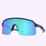 Oakley OO9463 06 39 Sutro Lite Unisex Sunglasses feature a large blue-green reflective lens, navy blue top frame, and Oakley branding on the arms. Shown against a light purple background.