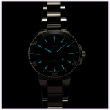 An Oris Watches Aquis Date metal-link wristwatch with glowing blue luminous hands and hour markers against a black background.