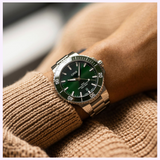 An Oris Watches Aquis Date stainless steel dive watch with a dark green dial and bezel, worn on a wrist.