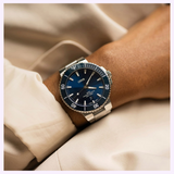 An Oris Watches Aquis Date dive watch with a blue face, rotating bezel, and stainless steel link bracelet worn on a wrist.