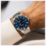 An Oris Watches Aquis Date stainless steel dive watch with a blue sunray dial and blue rotating bezel, worn on a wrist.