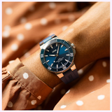 A dark blue Oris Watches Aquis Date dive watch with a matching rubber strap on a person’s wrist.