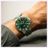 An Oris Watches Aquis Date diver’s watch with a green dial and bezel, worn on a matching green rubber strap on a person’s wrist.