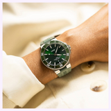 An Oris Watches Aquis Date stainless steel dive watch with a green dial and a matching green rubber strap worn on a person’s wrist.