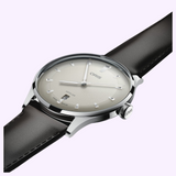 An Oris Watches Artelier Date watch featuring a silver case, a textured off-white dial with a date window at the six o’clock position, and a dark brown leather strap.