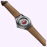 The back of an Oris Watches Artelier Date wristwatch revealing an automatic movement with a red oscillating weight and a tan leather strap.