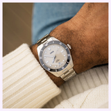 Oris Watches Divers Date wristwatch with a light dial, dark rotating bezel, and silver metal link bracelet, worn on a person’s wrist.