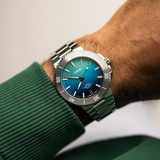 Oris Watches Great Barrier Reef Limited Edition IV wristwatch with a blue-to-green gradient dial, rotating bezel, and silver-tone metal bracelet worn on a wrist.