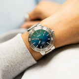 An Oris Watches Great Barrier Reef Limited Edition IV diver’s watch with a metallic bracelet and a blue-to-green gradient dial, worn on a wrist.