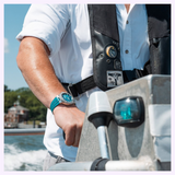 A person steering a boat while wearing an Oris Watches New York Harbor Limited Edition II watch with a teal dial and strap.