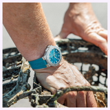 An Oris Watches New York Harbor Limited Edition II watch with a blue dial and rubber strap worn on a wrist resting on a wire mesh cage.