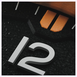 Macro view of an Oris Watches ProPilot Bronze dial featuring the numeral 12, a textured black surface, and orange indices beneath a bronze bezel.