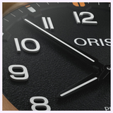 Close-up of an Oris Watches ProPilot Bronze watch dial featuring a black textured face, white Arabic numerals, and hands set to ten past ten.
