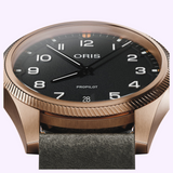 Close-up of an Oris Watches ProPilot Bronze watch with a black dial, white Arabic numerals, and a grey strap.