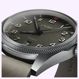 Close-up of an Oris Watches ProPilot Date watch featuring a textured grey dial, large numerals, black hands, a date window at six o’clock, a silver bezel, and a grey strap.