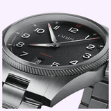 Close-up of an Oris Watches ProPilot Date wristwatch with a black textured dial, white numeral indices, and a stainless steel link bracelet.