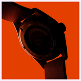 Close-up of an Oris Watches ProPilot Date case back featuring engraved text, including 10 bar and stainless steel, set against a solid orange background.