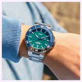 Oris Watches Yangtze Jiangtun Limited Edition wristwatch featuring a green wave-patterned dial, dark blue bezel, and silver metal link bracelet on a person’s wrist.