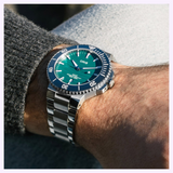 An Oris Watches Yangtze Jiangtun Limited Edition mechanical watch with a green gradient dial and a blue rotating bezel worn on a wrist.