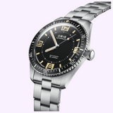 Oris Watches Divers 60th Anniversary Edition stainless steel watch featuring a black dial with luminous hands and beige numerals on a metal link bracelet.
