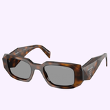 The PRADA Sunglasses 0PR 17WSF 20D50Q51 feature tortoiseshell rectangular frames and dark lenses, shown against a light purple background—a bold sporty style from Prada Sunglasses’ Linea Rossa collection.