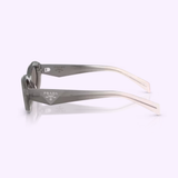 Side view of Prada Sunglasses 0PR 26ZS 20F80Q55 with a gray sporty design, featuring thick, angular arms and a prominent white Prada logo on the side; set against a softly lit background.